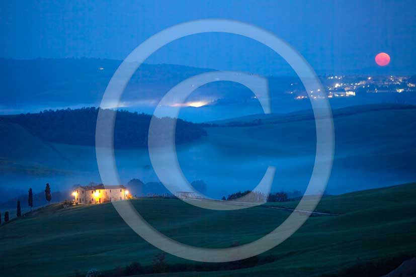 2010 - Night view of landscapes  with farm, fog and descending red moon upon S. Quirico Orcia village in spring, Orcia valley, near Pienza medieval village 21 miles south Siena province.